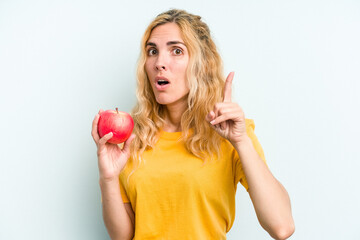 Young caucasian woman holding an apple isolated on blue background having an idea, inspiration concept.