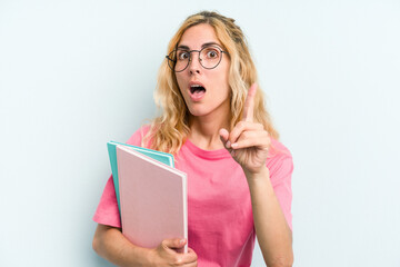 Young student caucasian woman holding books isolated on blue background having an idea, inspiration concept.