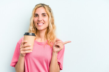 Young caucasian woman holding a take away coffee isolated on blue background smiling and pointing aside, showing something at blank space.