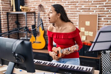 Young african american woman musician singing song playing ukelele at music studio