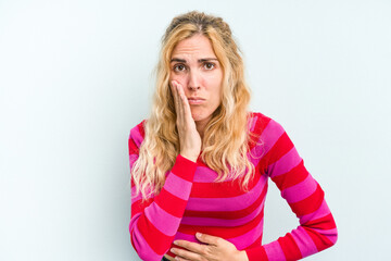 Young caucasian woman isolated on blue background blows cheeks, has tired expression. Facial expression concept.