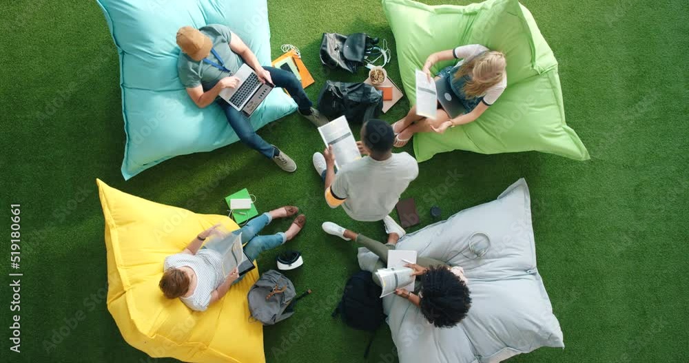 Poster above view of creative students collaborating on a project, sitting on bean bags in an office setup.