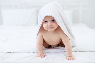 a baby in a white towel after bathing in a bathtub on a bright bed at home smiles, the concept of hygiene and washing