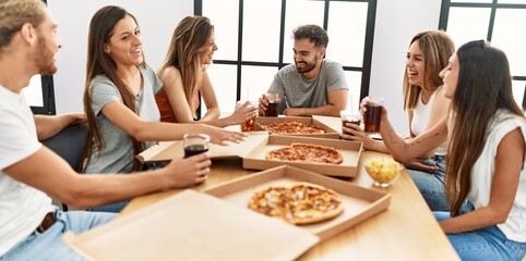 Group of young people smiling happy eating italian pizza sitting on the table at home