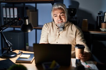 Middle age man with grey hair working at the office at night smiling cheerful offering palm hand giving assistance and acceptance.