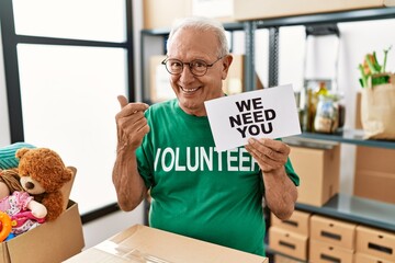 Senior volunteer man holding we need you banner smiling happy pointing with hand and finger to the side