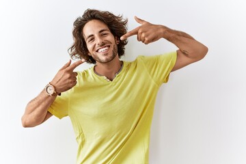 Young hispanic man standing over isolated background smiling cheerful showing and pointing with fingers teeth and mouth. dental health concept.