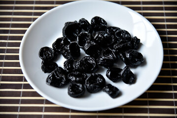 Dried prunes on a white plate close-up.