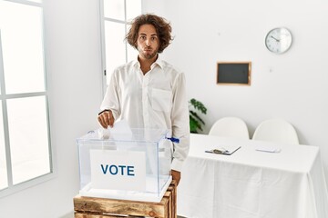 Young hispanic man voting putting envelop in ballot box depressed and worry for distress, crying...