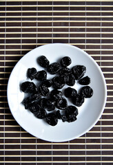 Dried prunes on a white plate close-up.
