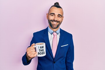 Young hispanic man drinking from i am the boss coffee cup looking positive and happy standing and smiling with a confident smile showing teeth