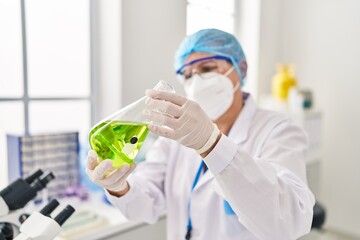 Middle age woman wearing scientist unifor and medical mask holding test tube at laboratory