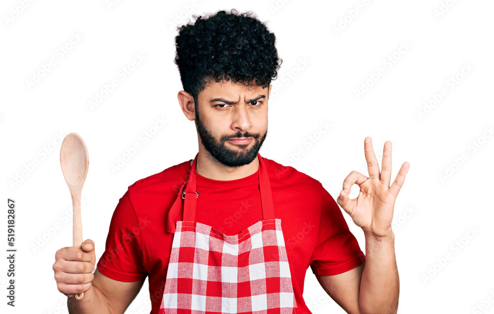 Sticker young arab man with beard wearing baker uniform holding wooden spoon skeptic and nervous, frowning u