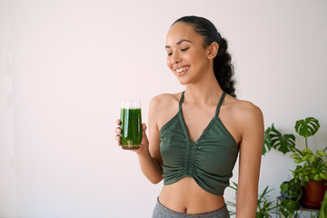 A beautiful multi-ethnic woman smiles with green juice - spinach, kale, vitamans - Powered by Adobe