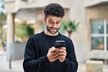 Young arab man smiling confident using smartphone at street - Powered by Adobe