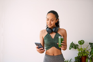 A young multi-ethnic woman tracks yoga session on fitness app with green juice - obrazy, fototapety, plakaty