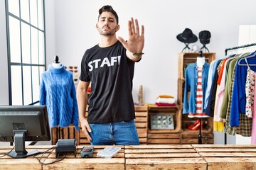 Young hispanic man working at retail boutique doing stop sing with palm of the hand. warning...