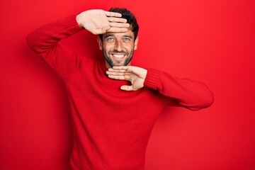 Handsome man with beard wearing casual red sweater smiling cheerful playing peek a boo with hands...