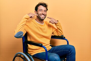Handsome man with beard sitting on wheelchair smiling cheerful showing and pointing with fingers teeth and mouth. dental health concept.