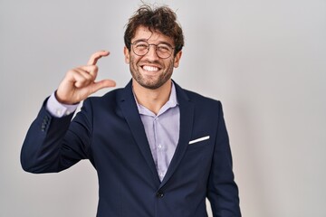 Hispanic business man wearing glasses smiling and confident gesturing with hand doing small size sign with fingers looking and the camera. measure concept.
