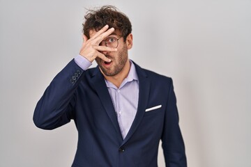 Hispanic business man wearing glasses peeking in shock covering face and eyes with hand, looking through fingers with embarrassed expression.