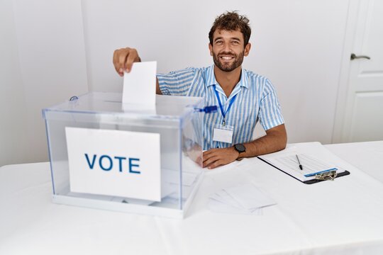 Young hispanic politic party worker smiling happy putting vote in ballot box at electoral college.