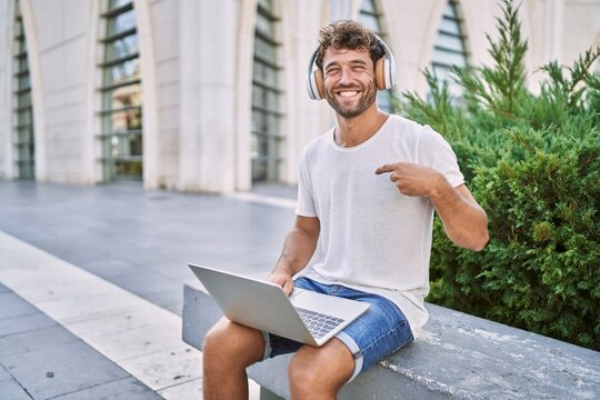 Young hispanic man using headphones and laptop at street pointing finger to one self smiling happy and proud