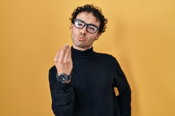 Hispanic man standing over yellow background doing italian gesture with hand and fingers confident expression