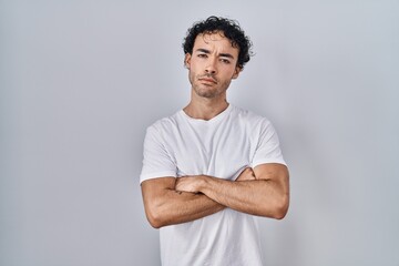 Hispanic man standing over isolated background skeptic and nervous, disapproving expression on face with crossed arms. negative person.