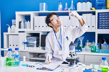 Fototapeta premium Young hispanic man scientist writing on document holding blood test tube at laboratory