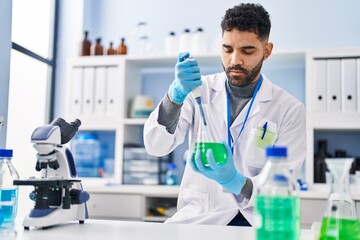 Young hispanic man wearing scientist uniform measuring liquid at laboratory