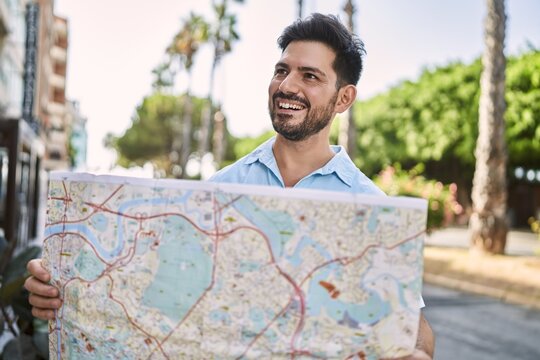 Young hispanic man smiling happy holding map at the city.