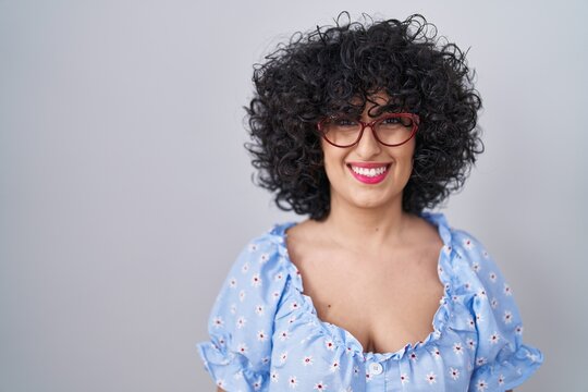 Young brunette woman with curly hair wearing glasses over isolated background with a happy and cool smile on face. lucky person.