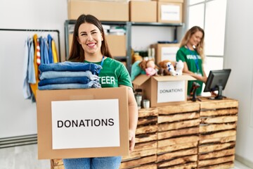 Two volunteers woman working at charity center. Girl smiling happy and holding box with clothes to donate.