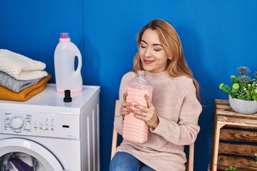 Young woman smelling detergent waiting for washing machine at laundry room