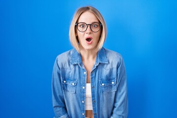 Young caucasian woman standing over blue background afraid and shocked with surprise expression, fear and excited face.