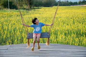 Little asian child on swing and looking up at yellow flowers background