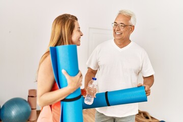 Middle age hispanic sporty couple smiling happy holding yoga mat at sport center.