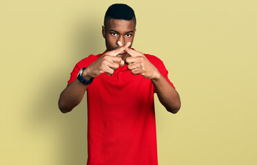 Young african american man wearing casual red t shirt rejection expression crossing fingers doing negative sign