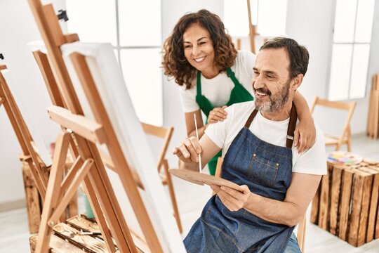 Middle age student and teacher smiling happy painting at art school.