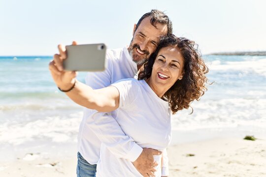 Middle age hispanic couple smiling happy and hugging making selfie by the smartphone at the beach.