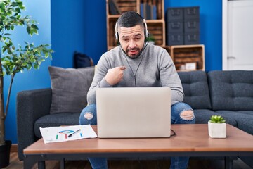 Hispanic man using laptop working from home pointing finger to one self smiling happy and proud