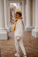 Beautiful woman dressed white jeans, sweater and yellow scarf and beret walking in the street of the city. fthe fall urban style fashion concept
