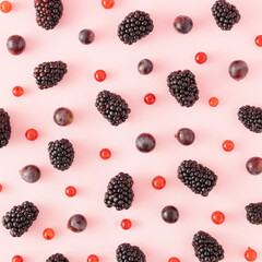 Creative minimal pattern made of ripe blackberries, currants and black fragrant grapes on a pink background. Minimal flat lay concept. Summer, berries and fruit inspiration.