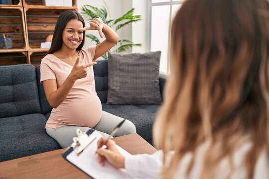 Young pregnant woman at therapy session smiling making frame with hands and fingers with happy face. creativity and photography concept.