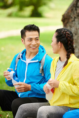 Positive young man talking to girlfriend and drinking water after long bicycle ride