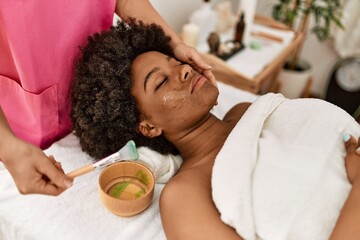 Obraz na płótnie Canvas Young african american woman having facial treatment at beauty center