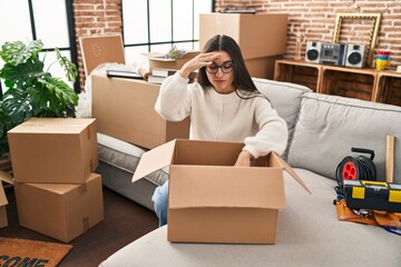 Young hispanic woman worried unpacking cardboard box at new home