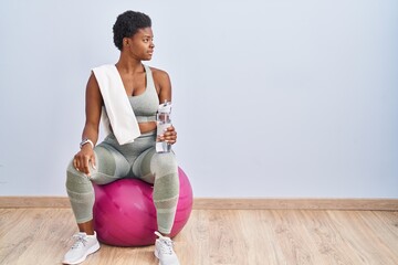 African american woman wearing sportswear sitting on pilates ball looking to side, relax profile...