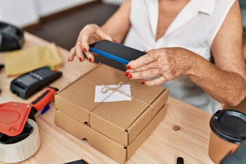 Senior grey-haired woman business worker make photo to package order at office